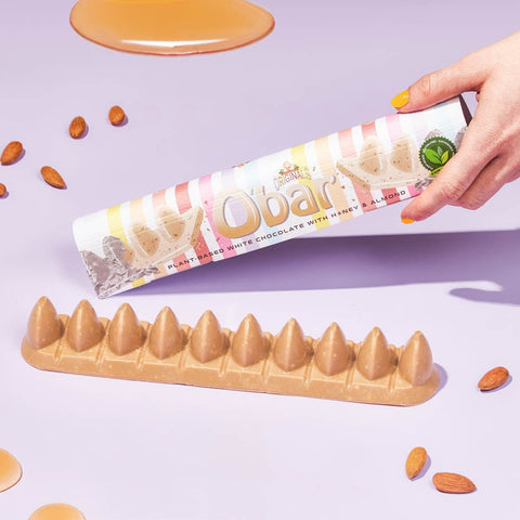 Obar chocolate bar with almond pieces and liquid honey on a light purple background.