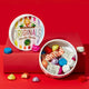 Catherine's Originals chocolate selection in a round tin, shown open with assorted foil-wrapped chocolates and candy pieces spilling out, next to the branded lid on a red background.