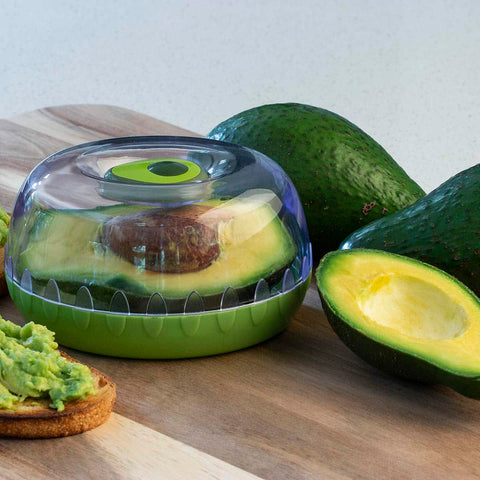 Avocado in the fresh keeper pod on a wooden board with avocado toast to the side.