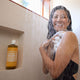 Woman showering with a bottle of Dr. Bronner's 18-in-1 Pure-Castile Magic Soap - Citrus in the shower niche.