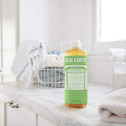 Bottle of Dr. Bronner's 18-In-1 Pure Castile Soap on a marble counter with a laundry basket in the background.