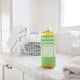 Bottle of Dr. Bronner's 18-In-1 Pure Castile Soap on a marble counter with a laundry basket in the background.