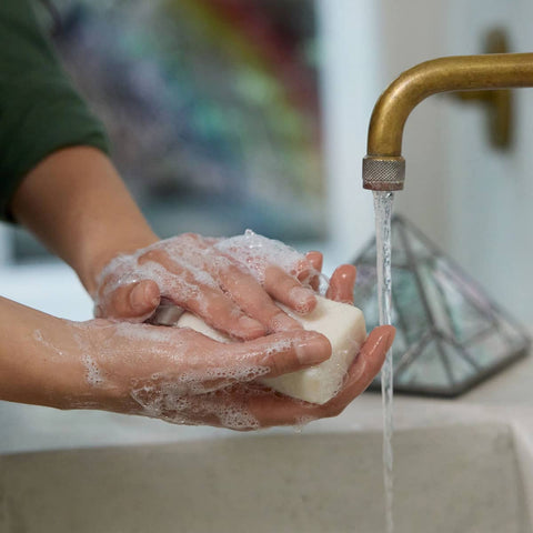 Person washing hands with Dr. Bronner's Pure-Castile Magic Soap Bar - Rose 140g under a running faucet.