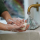Person washing hands with Dr. Bronner's Pure-Castile Magic Soap Bar - Rose 140g under a running faucet.
