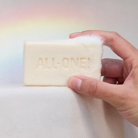 Bar of soap with 'ALL-ONE!' branding held by a hand against a gradient background.