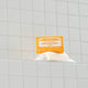 Bar of soap with a yellow label on a tiled bathroom shelf.