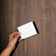 Hand holding a blank white card against a wooden background.