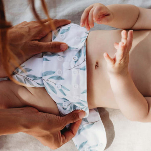 Mum adjusting snaps of cloth nappy on her baby. 