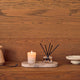 Candle and diffuser on a marble tray against a wooden wall.