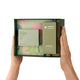 Two hands holding an open dark green Endota Organics gift set box against a white background. The box contains a coffee sea salt body guide and a Signature Blend Body & Massage Oil.