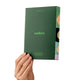A hand holding a dark green Endota mask set box against a solid white background. The box features the brand name 'endota' in light green text and displays a colourful side panel with abstract circular patterns.