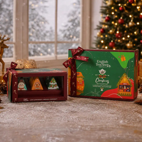 English Tea Shop Christmas Tea Collection gift box set displayed on a snowy floor in front of a window and decorated Christmas tree.