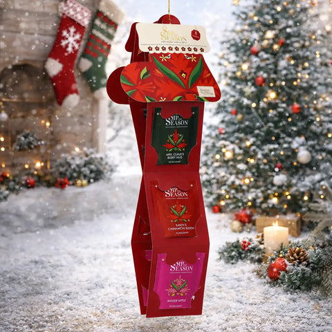 A red Christmas gift box display stand filled with seasonal packaged items, photographed in a snowy holiday scene.