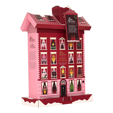A pink and red cardboard advent calendar shaped like a multi-story house with illustrated windows.