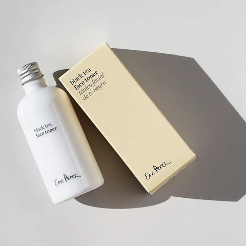 A white bottle of Black Tea Face Toner next to its beige packaging box, styled on a light gray surface with a soft shadow.