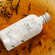 White bottle of Black Tea Face Toner in an orange liquid, surrounded by tea leaves.