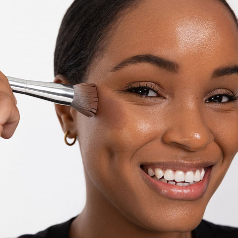 Woman applying Ere Perez Cacao Bronzing Pot - Costa 7.5g makeup product with a brush.