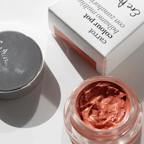 Open cosmetic jar with metallic pink cream and closed lid on a white background