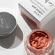 Open cosmetic jar with metallic pink cream and closed lid on a white background
