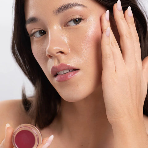 Woman applying ere perez carrot colour pot in the shade 'holy', to her cheek & lips. 