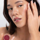 Woman applying ere perez carrot colour pot in the shade 'holy', to her cheek & lips. 