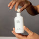 Person holding a white bottle labeled 'Ere Perez ginkgo micellar cleanser 37g' with a dropper, against a gray background.