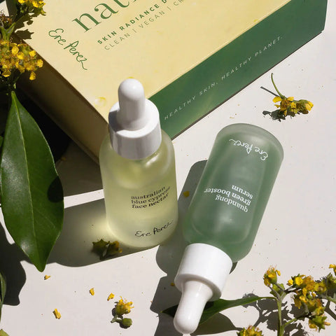 Two native glow bottles with droppers next to packaging on a light surface with green leaves and flowers.
