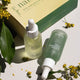 Two native glow bottles with droppers next to packaging on a light surface with green leaves and flowers.