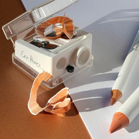 Perfect catch duo sharpener and makeup pencils on white and wooden surface.