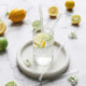 Ever Eco glass drinking straws styled in a glass of sparkling water with lemon and lime slices and flowers placed around. Sitting on a white coaster on a marble surface.