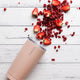 Ever Eco light pink insulated tumbler laid on its side on a white wooden surface with sliced strawberries, pomegranate & frozen raspberries artistically placed to look as though they're spilling out.