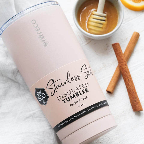 Stainless steel insulated tumbler on a white tea towel styled next to a couple of cinnamon sticks & honey in a bowl.