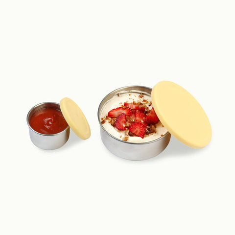 Buttercup yellow silicone lids and stainless steel snack pods. Small size filled with sauce. Bigger size filled with yoghurt, strawberries & granola.