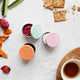 3 stainless steel containers filled with dips on a kitchen surface with snack foods.