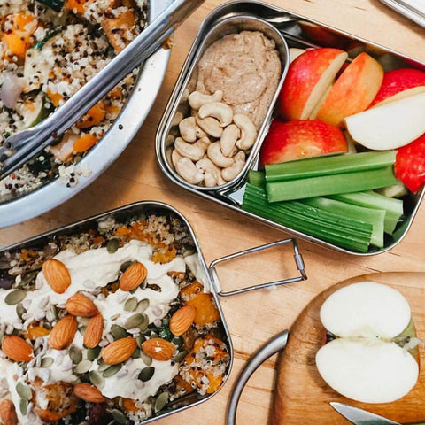 Two stainless steel bento boxes packed with food on a wooden surface.