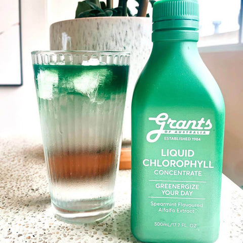 Green bottle of Liquid Chlorophyll next to a glass of water.