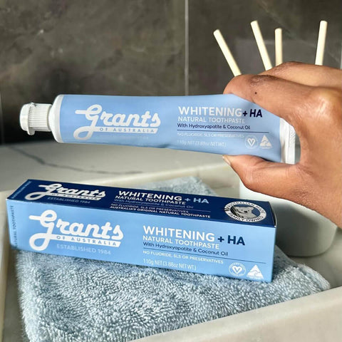 Hand holding a tube of Grants Whitening +HA toothpaste with packaging in the foreground.