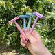 Hand holding four colourful razors against a green outdoor background.