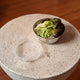 A clear silicone lid placed beside a stainless steel bowl filled with mixed green and purple lettuce on a speckled stone table.