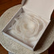 A coiled translucent white silicone strap or band, neatly arranged inside an open white cardboard box, placed on a speckled stone table.