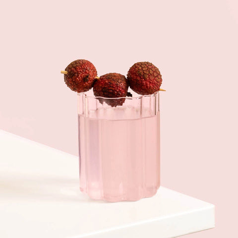 Stylish wavy glass of light pink protein water with lychees on a pink background.