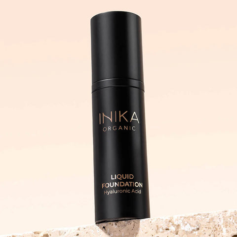 Black bottle of INIKA Organic Liquid Foundation on a beige background.