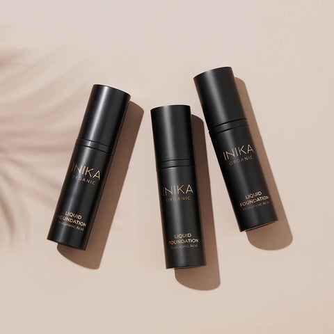 Three bottles of INIKA Organic Liquid Foundation on a beige background.