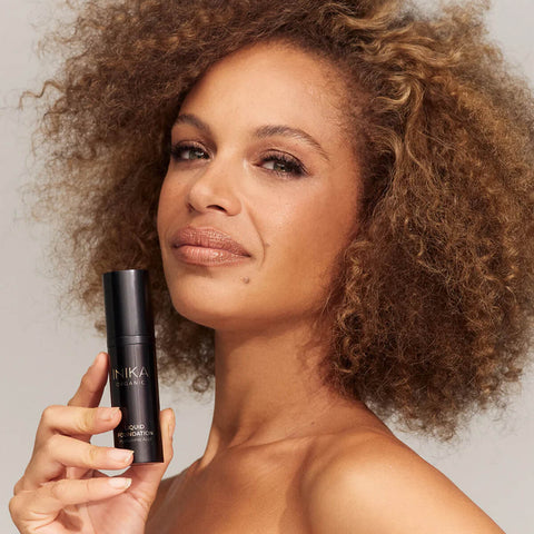 Woman with curly hair holding bottle of INIKA Organic Liquid Foundation.