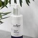 Juniper Calming Jojoba Moisturiser bottle on a light background with green leaves.