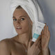 Woman with a towel wrapped around her head holding a 'Juniper' skincare product.