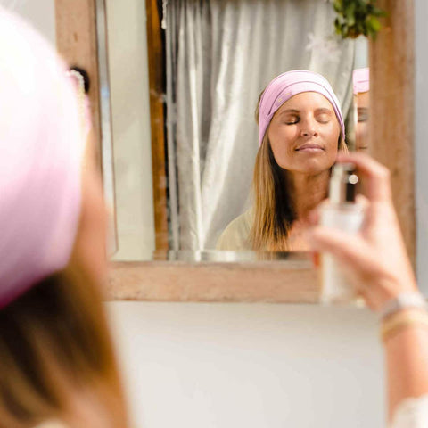 Woman applying a product to her face in front of a mirror.