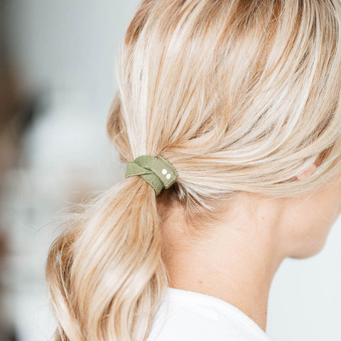 Close-up of blonde hair tied with a green hair tie against a blurred background