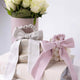 Pumice Stone and Violet Ice Plastic-Free Satin Bows, on a light surface with flowers in the background.