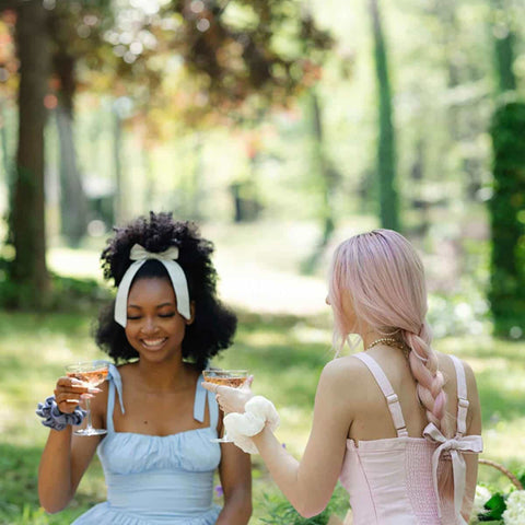 Two women having a picnic sharing a glass of bubbles and wearing kooshoo's plastic free bows and scrunchies. 